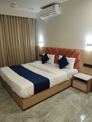 A hotel room with a large bed, a nightstand, an air conditioning unit, and a curtain. - Hotel Earth Orbit (Gandhinagar)