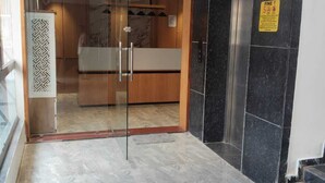 Un vestíbulo de hotel con entrada por puerta de vidrio, mostrador de recepción, perchero y un cartel que indica multa por no fumar.