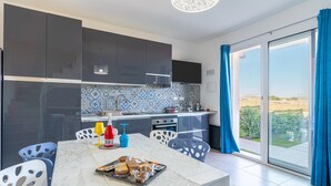 A modern kitchen with dark cabinets, a tiled backsplash, and a dining area with a table set for two. - Apartment 'I Due Mori Marzamemi' with Sea View, Wi-Fi and Air Conditioning (Marzamemi)