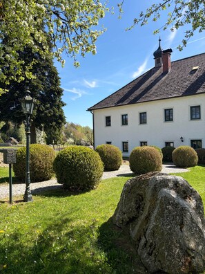 A white building with a slate roof, surrounded by well-maintained hedges and a stone pathway.
