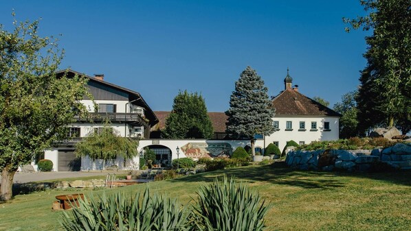 Ein großes, weißes Gebäude mit traditionellem Dach und einem Glockenturm, umgeben von einem gepflegten Garten und Bäumen.