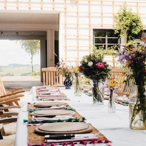 Een gedekte tafel voor een maaltijd, met stoelen, vazen met bloemen en uitzicht op het buiten.