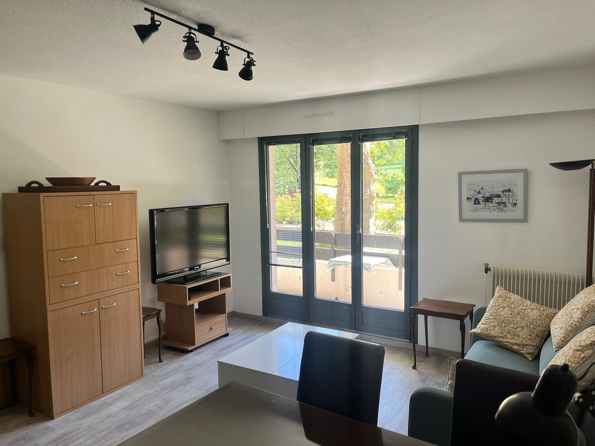Een moderne woonkamer met een flatscreen televisie op een houten standaard, een bank, een salontafel en een kast.