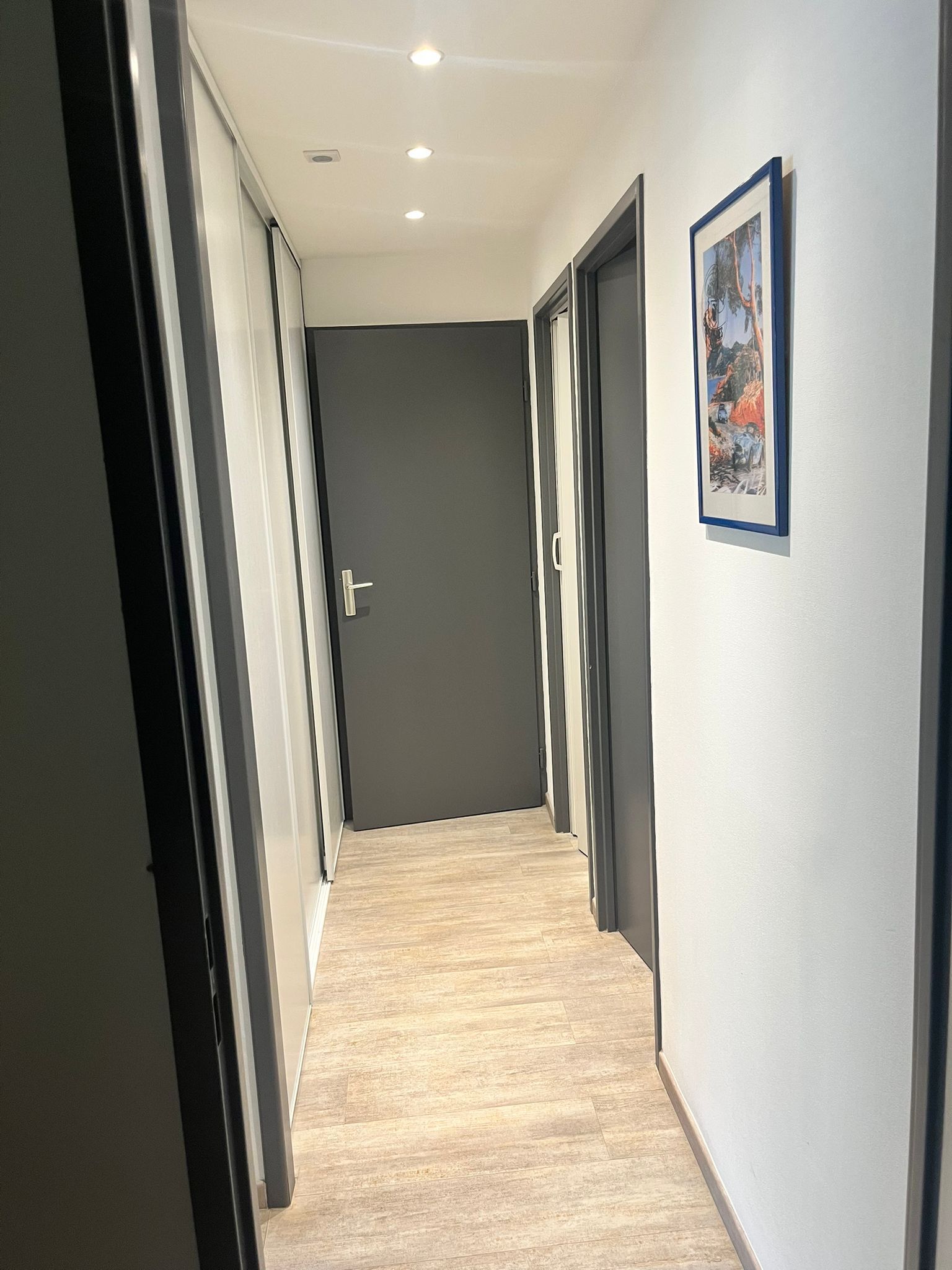 Um corredor com piso de madeira, paredes cinzentas e uma porta no final.