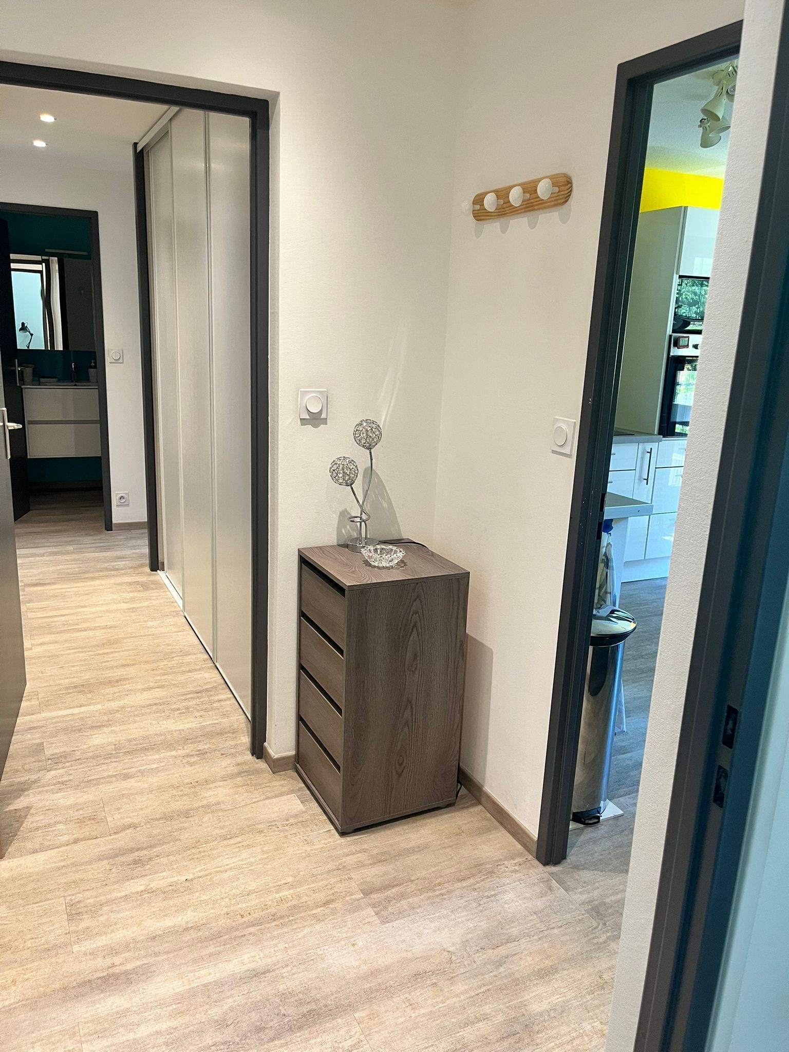 Een hal met een houten vloer, een klein houten kastje met lades, en een wandlamp.