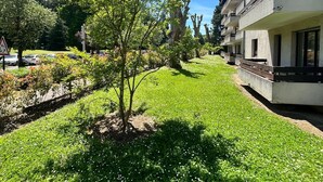 Un barrio residencial con un árbol pequeño, un césped cuidado y un edificio de varios pisos con balcones.