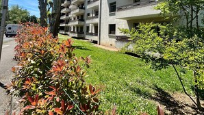 Un edificio residencial de varios pisos con balcones, rodeado de follaje y árboles bien cuidados.
