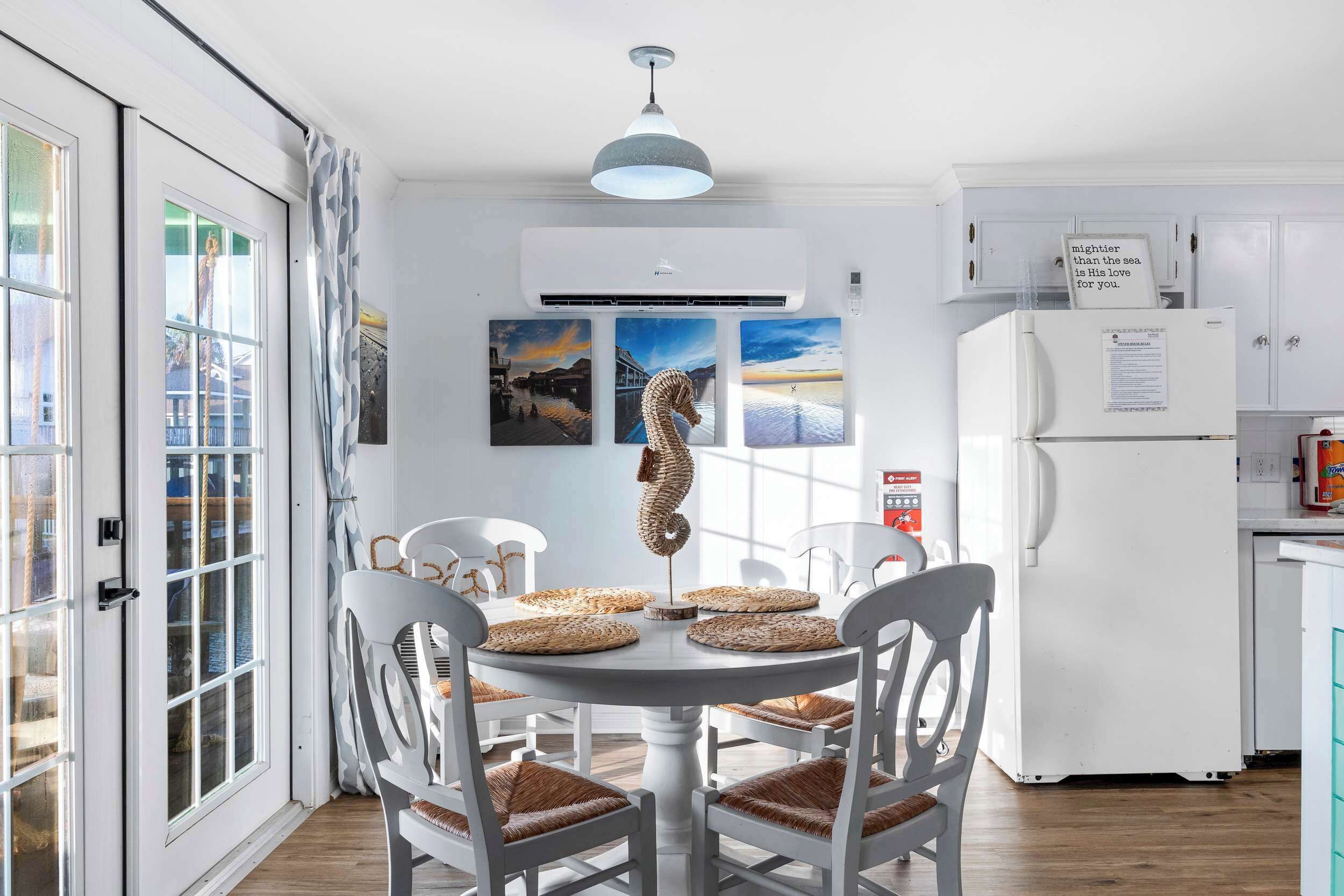 A dining area with a round table, four white chairs, and a hanging light fixture.