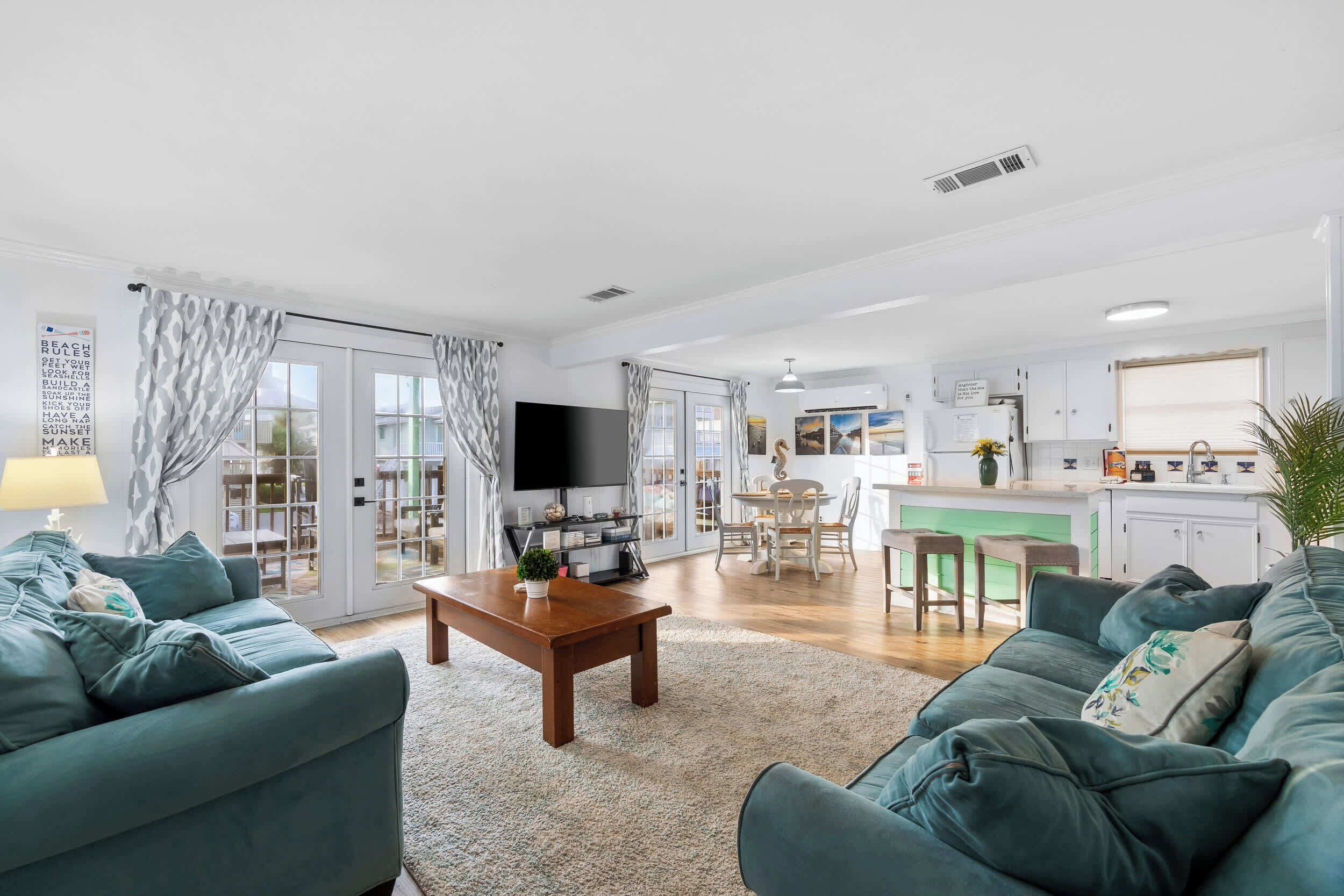 A modern living room with a flat-screen TV, two sofas, a coffee table, and a kitchen area with a dining table and chairs.