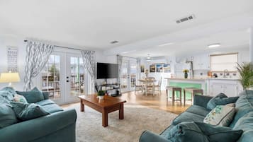 A modern living room with a flat-screen TV, two sofas, a coffee table, and a kitchen area with a dining table and chairs.