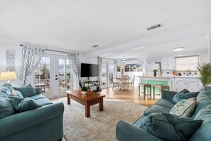 Ein modernes Wohnzimmer mit Flachbildfernseher, zwei Sofas, einem Couchtisch und einer Küchenzeile mit Esstisch und Stühlen.