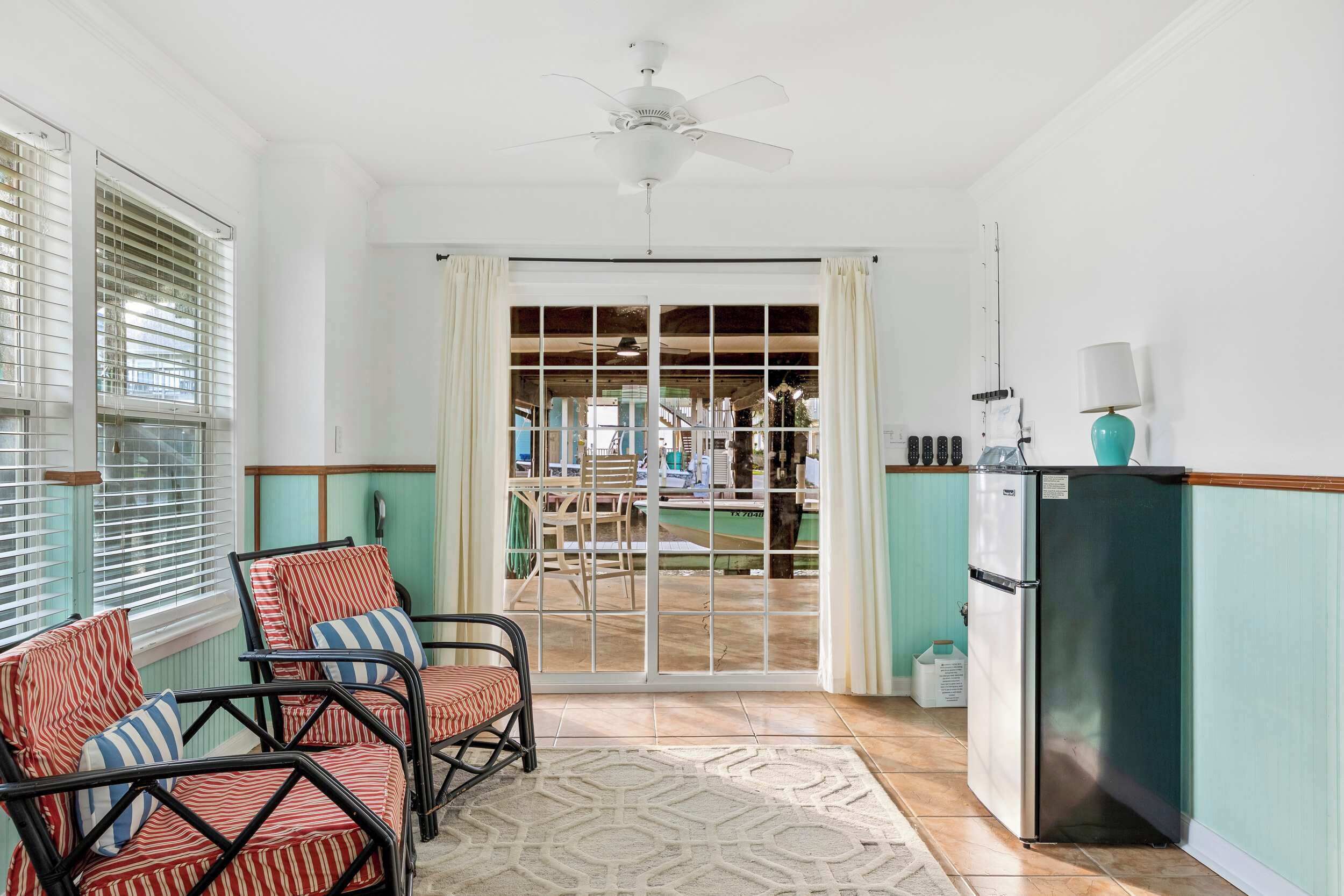 A room with a ceiling fan, a sliding glass door leading to an outdoor area, a refrigerator, and a chair with striped cushions.