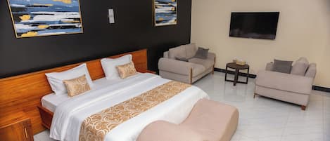 A hotel room with a large bed, two armchairs, a small table, and a TV on the wall.