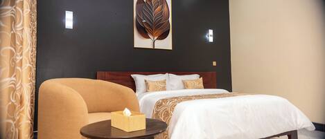 A hotel room with a bed, a chair, a bedside table with a tissue box, a wall-mounted air conditioner, and a framed leaf artwork.