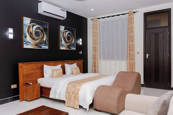 A modern bedroom with a wooden bed, a nightstand, a sofa, and two abstract paintings on the wall. - DEEL Comfort Inn (Dar es Salaam)