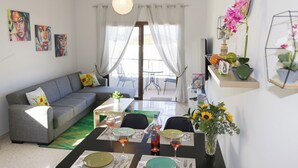 Un soggiorno moderno con un divano, un tavolo da pranzo e sedie. Alle pareti si vedono dipinti, un vaso con fiori e una TV su un mobile.