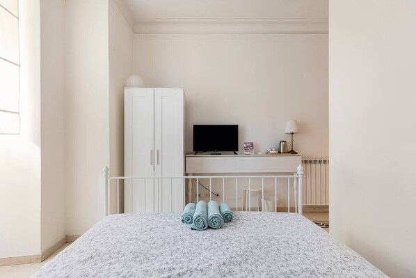 A bedroom with a bed, a desk with a TV, a wardrobe, and a radiator. - White - Comfy double room with private bath in the cutest area of Rome (Roma)