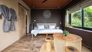 Ein Schlafzimmer mit einem Bett, einem Deckenventilator, einem runden Holztisch und Blick auf Grünflächen.