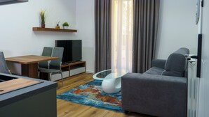 Una sala moderna con una mesa de centro de vidrio, un sofá gris, una mesa de comedor de madera y un televisor de pantalla plana.