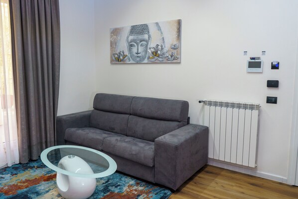 En moderne stue med en grå sofa, et glasbord, et Buddha-maleri, en radiator og en termostat.