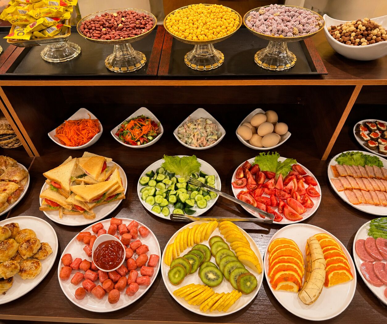 A buffet with various food items including sandwiches, salads, fruits, and nuts.