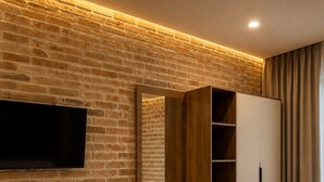 Habitación de hotel con pared de ladrillo, televisión de pantalla plana, estanterías de madera, armario y dos camas.