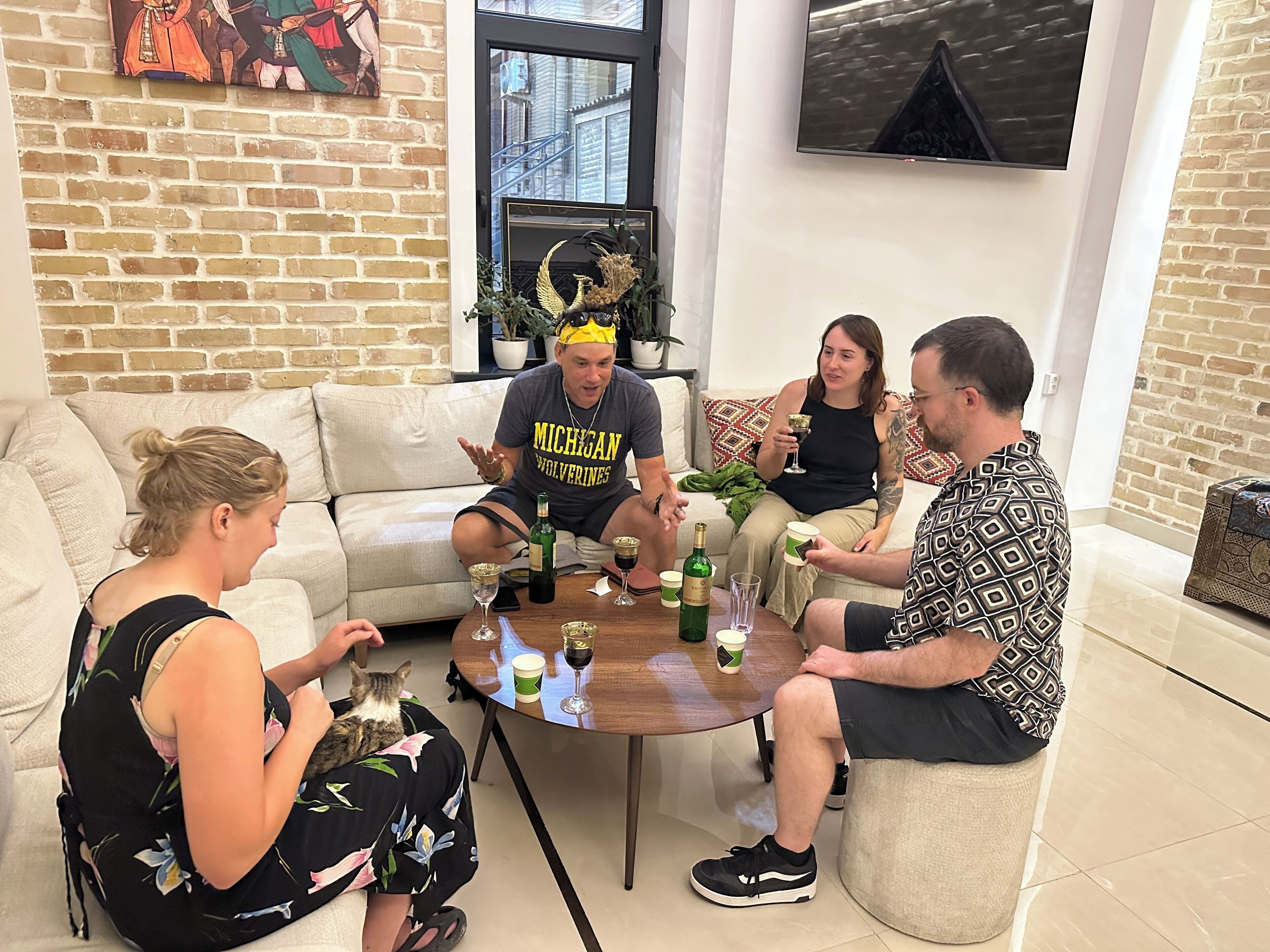 A group of people seated around a round table in a room with a brick wall and a window.