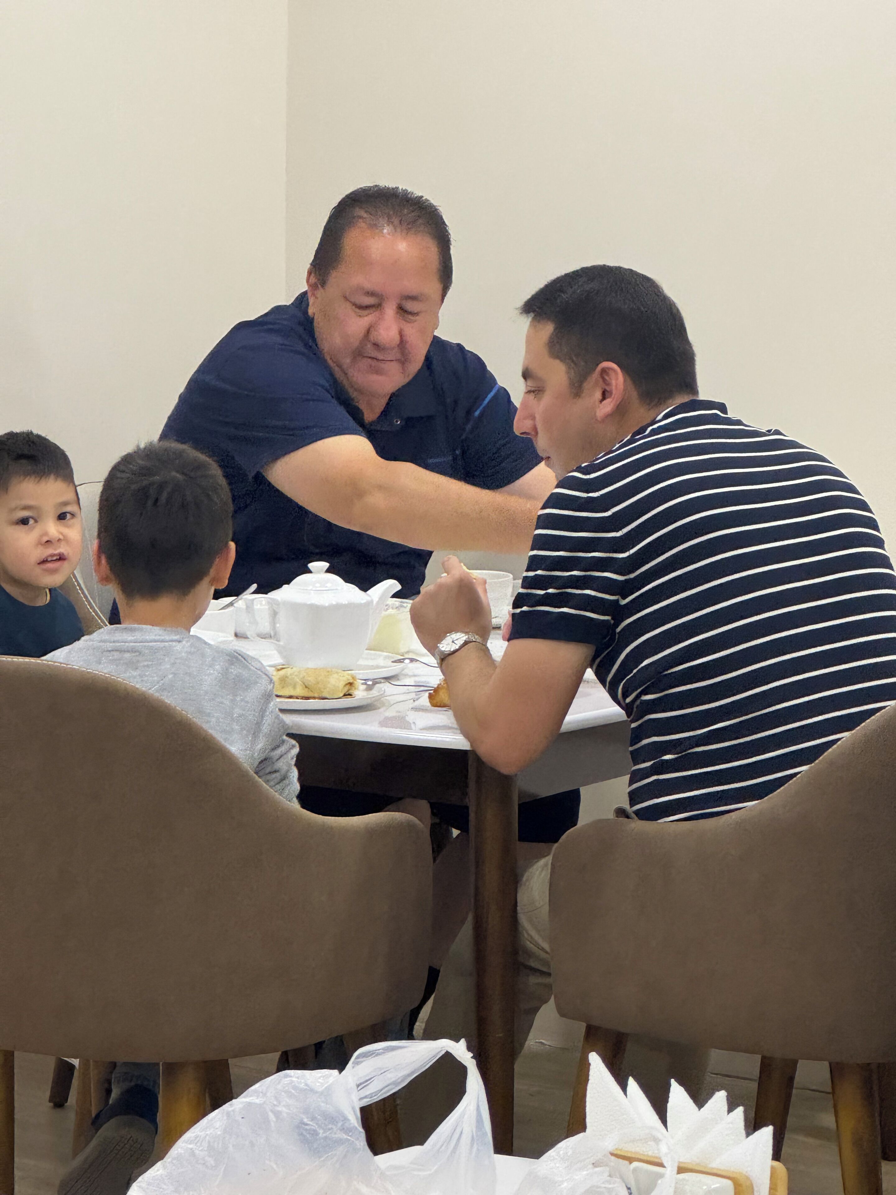 Uma mesa de jantar com cadeiras, toalha branca e alguém servindo comida para outra pessoa.