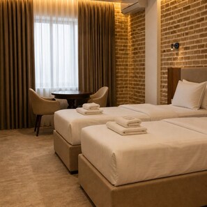 A hotel room with two beds, a round table, a chair, and a brick wall. - Shahristan Art Boutique Hotel (Samarkand)