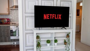 Un salon avec un meuble de rangement blanc pour l’équipement audiovisuel, un téléviseur à écran plat, et une cuisine en arrière-plan.