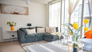 Un salon moderne avec un canapé d’angle, une table basse et une grande fenêtre agrémentée de rideaux.
