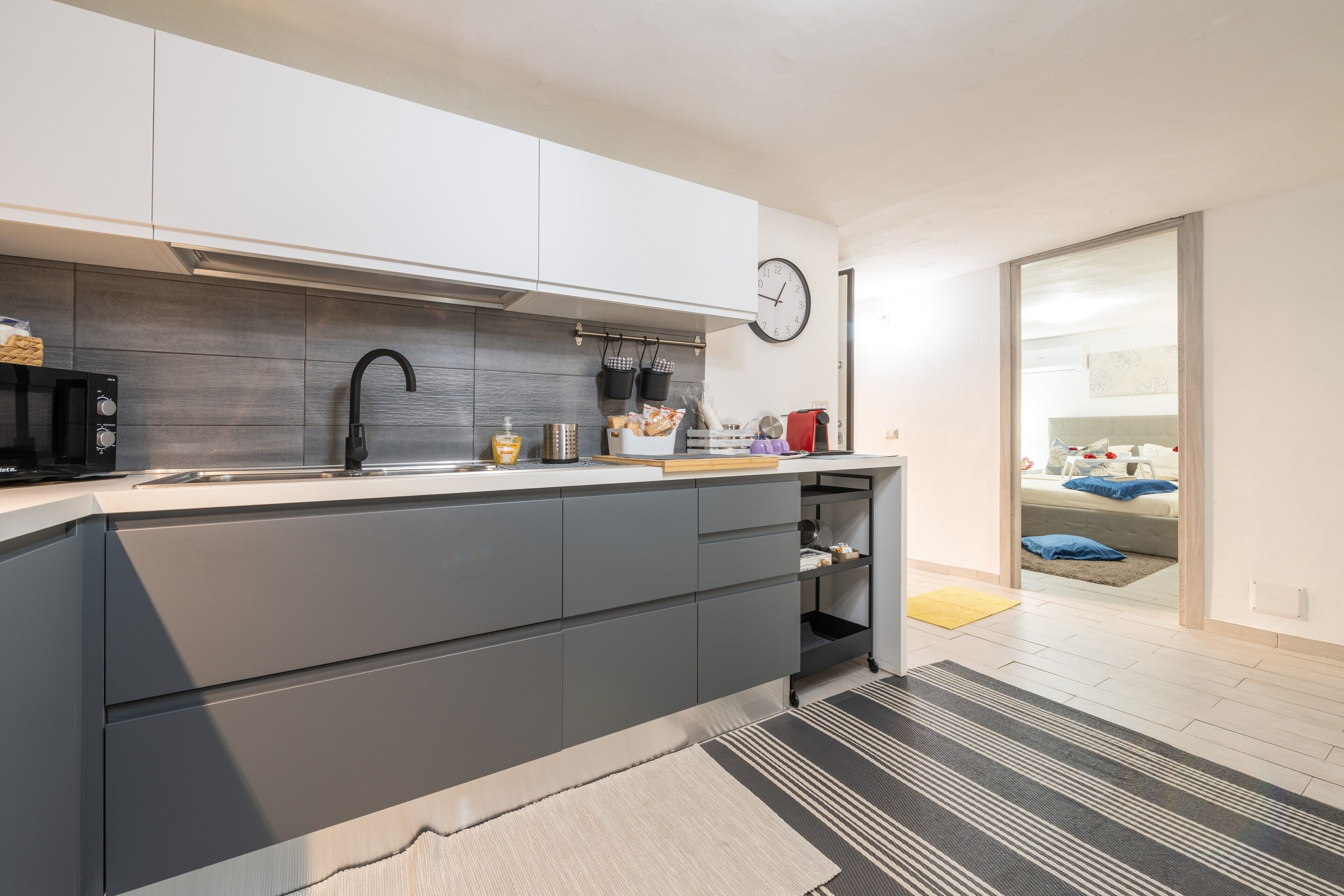 Een moderne keuken met grijze kastjes, een zwarte kraan en een klok aan de muur.