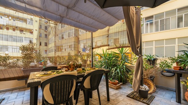 Une terrasse avec une table et des chaises, entourée de plantes en pot et offrant une vue sur un bâtiment.