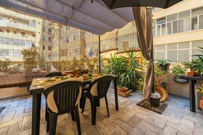 Une terrasse avec une table et des chaises, entourée de plantes en pot et offrant une vue sur un bùtiment.