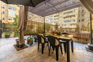 An outdoor patio with a table and chairs, surrounded by potted plants and a view of a residential building.