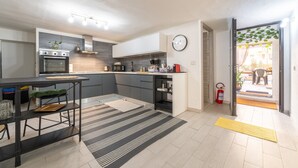 Une cuisine moderne dotée d’un four encastré, un coin repas avec une table et des chaises, et une vue sur l’extérieur grâce à une porte ouverte.