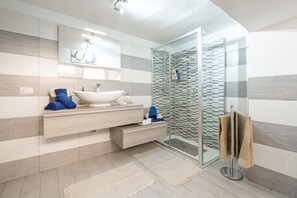 A modern bathroom with a glass shower enclosure, a white sink, and a large mirror.