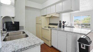 A kitchen with a granite countertop, white cabinets, a black microwave, a beige stove, and a window with a view of trees. - Apt. In college Station TX Mins to major hospitals and A&M U (College Station)