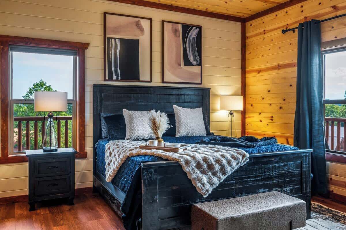 Una camera da letto con una testiera in legno, un letto con coperta blu, un comodino con una lampada e due quadri astratti incorniciati appesi al muro.