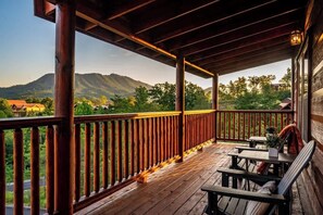 A wooden deck with a railing, a table, and chairs, overlooking a mountainous landscape. - 6-Bedroom Cabin with Indoor Pool & Hot Tub, Sleeps 24, Near Gatlinburg (Sevierville)