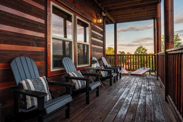 A wooden deck with Adirondack chairs and a table, overlooking a natural landscape.