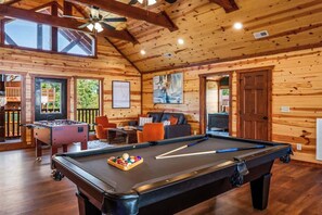 A wooden interior with a pool table, foosball table, and a sofa.