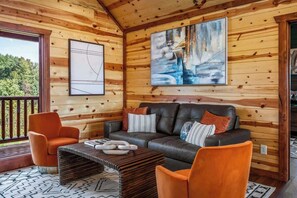 A wooden cabin interior with a sofa, two chairs, a coffee table, and artwork on the walls. - 6-Bedroom Cabin with Indoor Pool & Hot Tub, Sleeps 24, Near Gatlinburg (Sevierville)