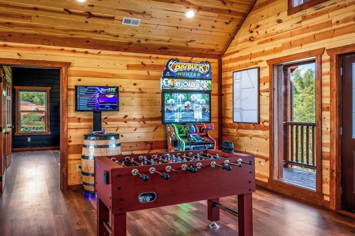 Un interior de madera con una mesa de fútbol de mesa, un televisor mostrando un partido y un letrero para el juego Big Buck Hunter.