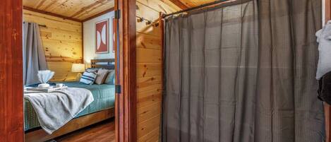 Een houten cabinestijl interieur met een bed, een badkamer met douchegordijn en een zichtbare deur.