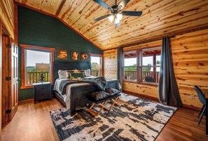 Une chambre à coucher comprenant un lit, un bureau, une chaise, un ventilateur de plafond et de grandes fenêtres.