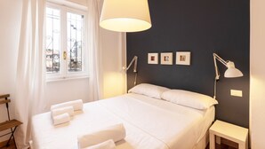 A neatly made bed with white linens and towels, a bedside lamp, and a window with curtains. - Two-room Apartment Peace Arch - Mirable PM (Milano)