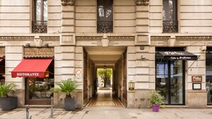 A building with a central entrance, potted plants, and storefronts labeled "La Tavernadei Golosi" and "Poku." - Two-room Apartment Peace Arch - Mirable PM (Milano)