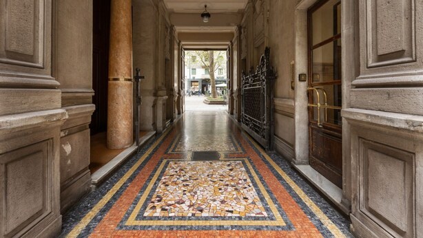 A corridor with a tiled floor, columns, and a door with a metal gate. - Two-room Apartment Peace Arch - Mirable PM (Milano)