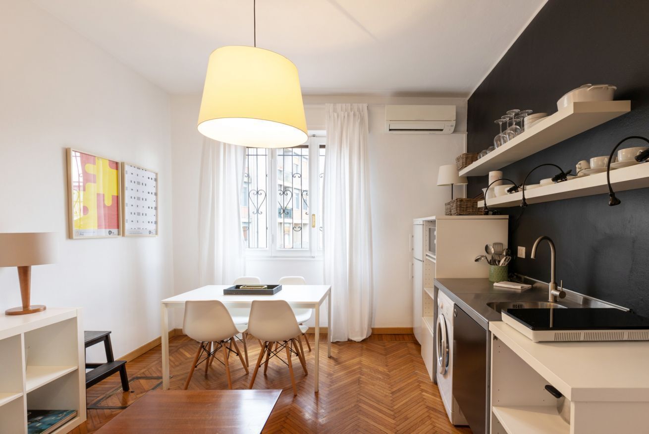 A modern kitchen with white cabinetry, a black backsplash, and a hanging light fixture.